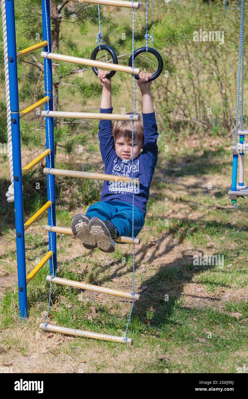 Kids Using Playground Rings A blonde-haired child is playing on the playground, hanging on rings ...