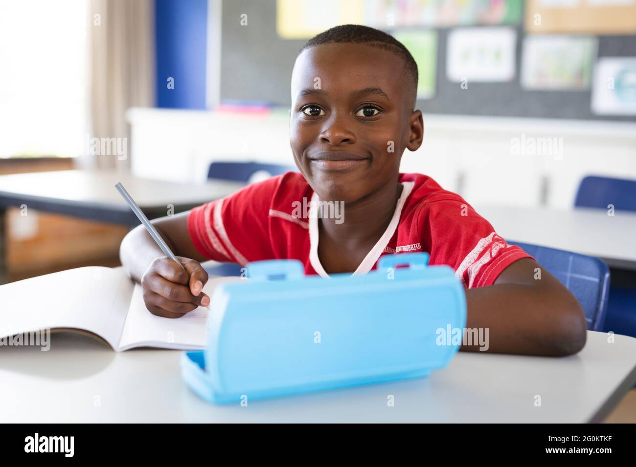 Portrait of african american boy smiling while sitting on his desk in ...