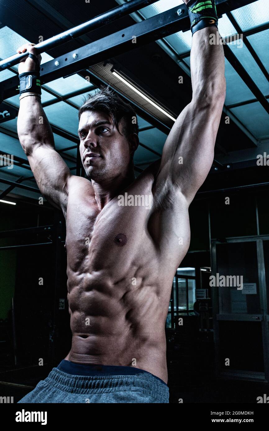 Vertical shot of a fit male bodybuilder hanging from a bar at the gym