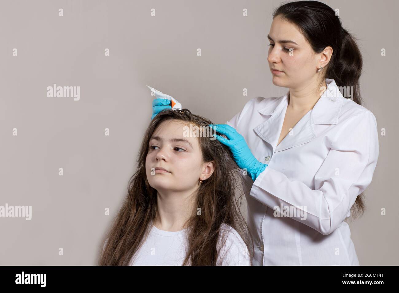 A dermatologist or trichologist applies a dandruff or lice weed to the patient's hair. Treating psoriasis, hair loss, dermatitis or head lice. Stock Photo
