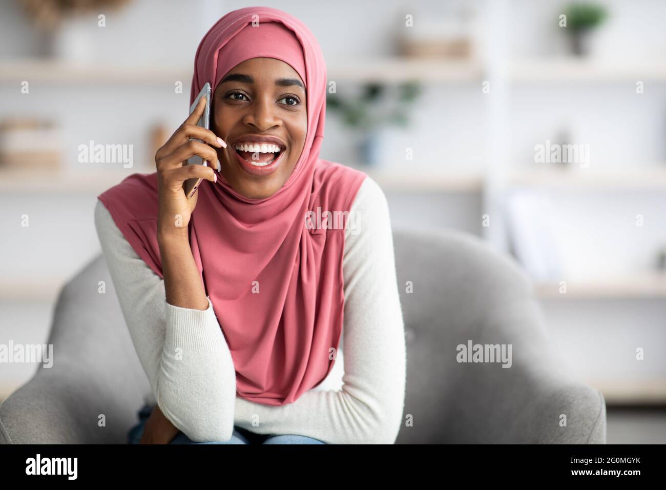 Cheerful Black Islamic Woman In Hijab Talking On Mobile Phone At Home ...