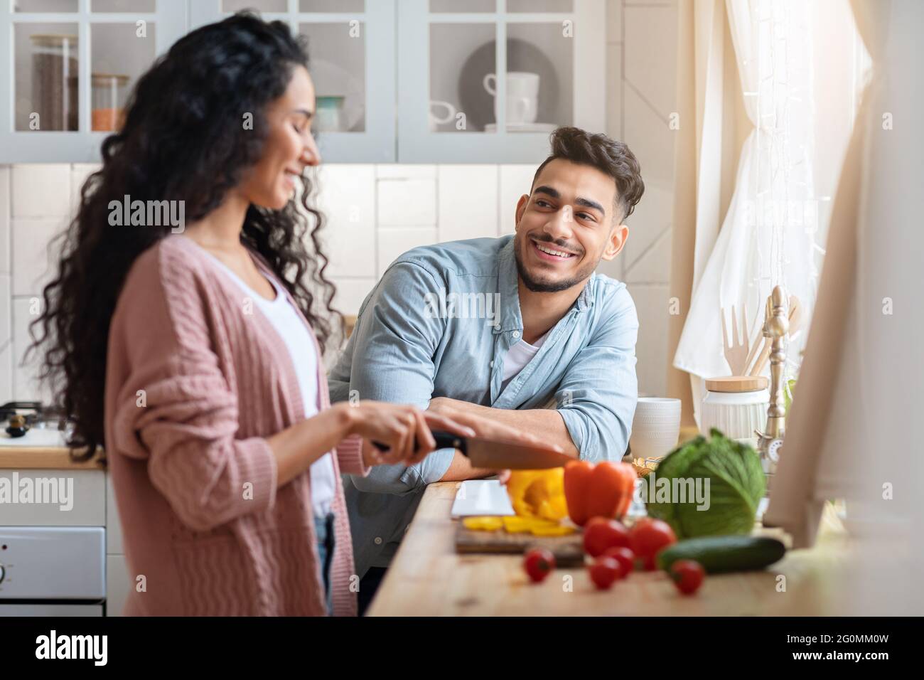 Loving Arab Man Looking At Wife While She Cooking Lunch In Kitchen Stock Photo