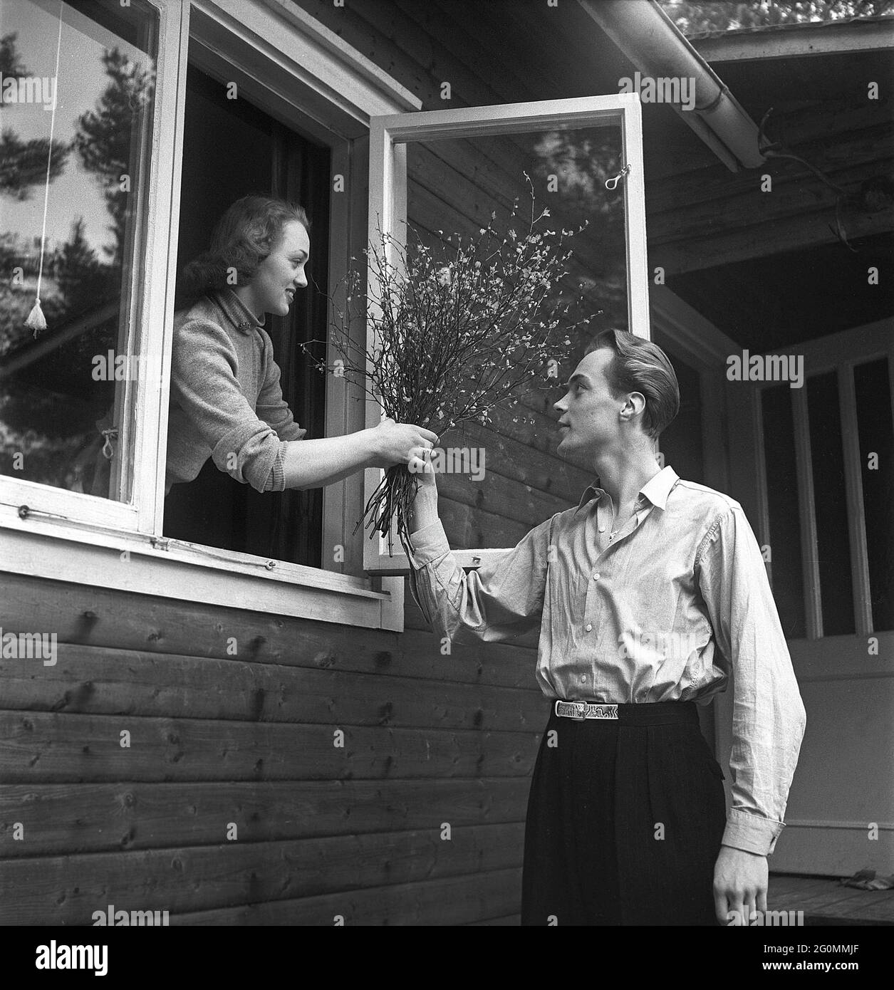 Lifestyle in the 1950s. A young couple pictured at their house. He is handing her a bouquet of branches with small leafs on it through the open window.   Sweden 1951 ref BB80-1 Stock Photo