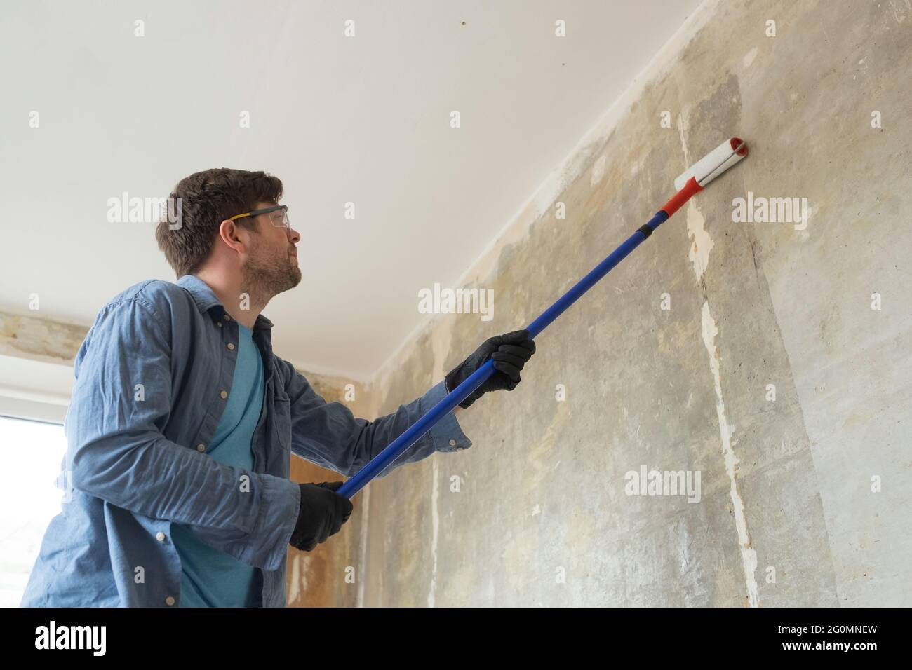 Caucasian man painting cement walls using roller brush and primer