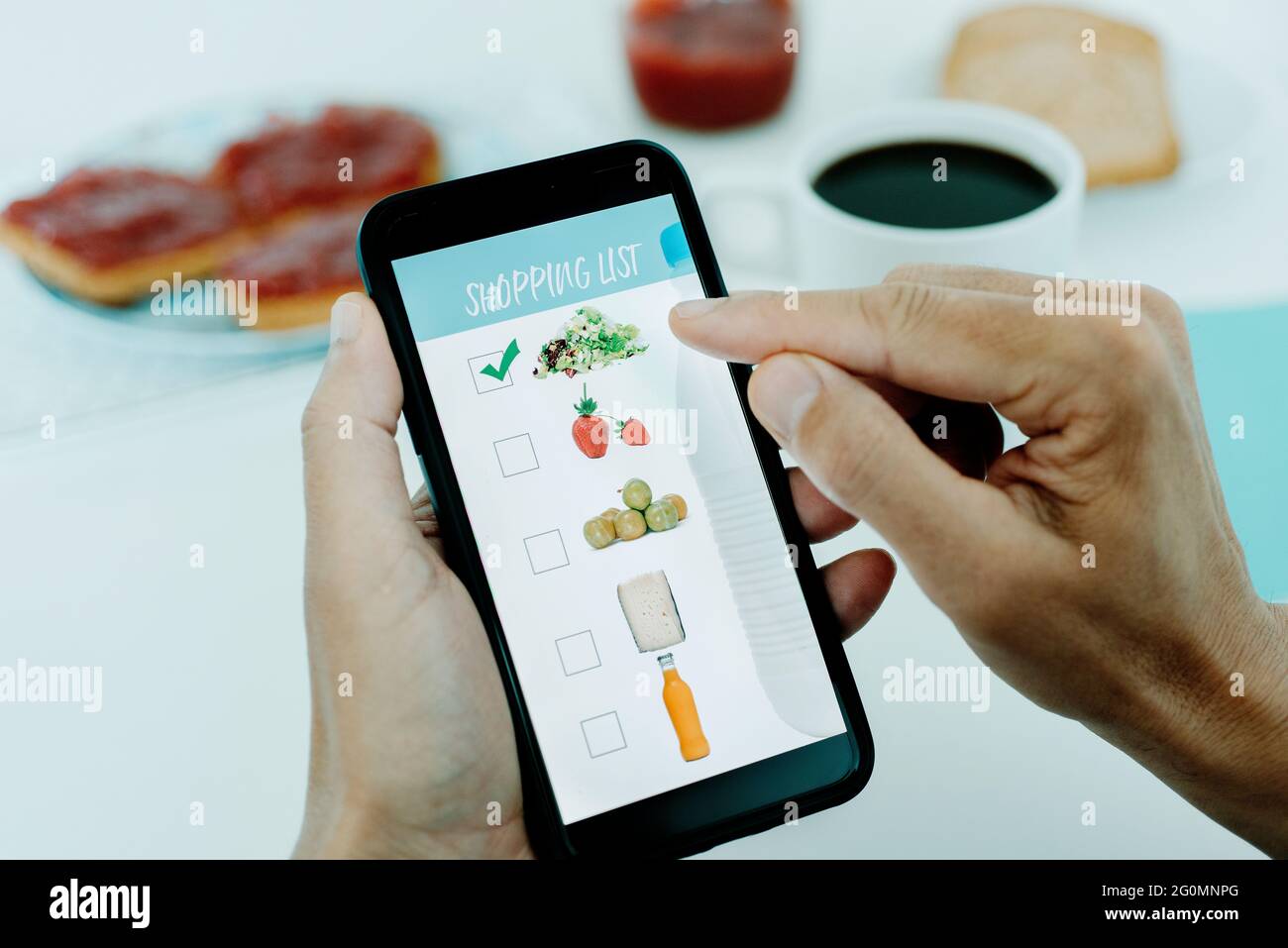 closeup of a young caucasian man, sitting at a table for breakfast, making his shopping list in his smartphone, with pictures of different products ma Stock Photo