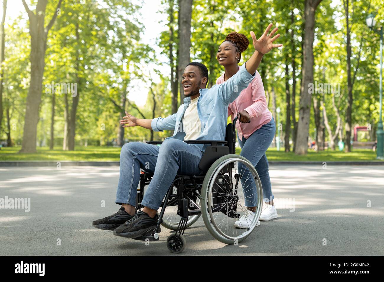 Happy black disabled guy in wheelchair on walk with his loving