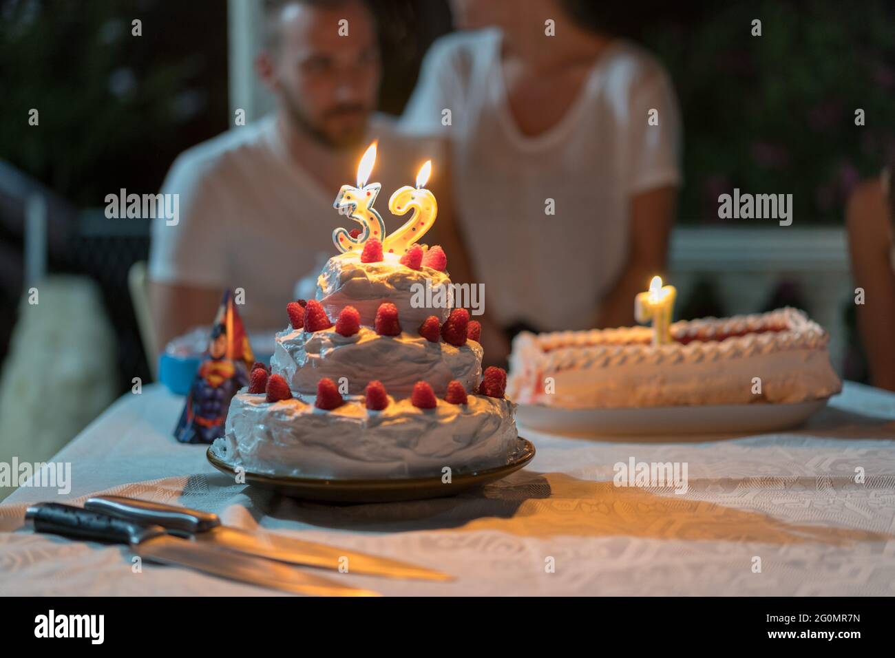 Guy celebrating his 32nd birthday. Cake with strawberries and fruit. Knives and party hats on the table Stock Photo