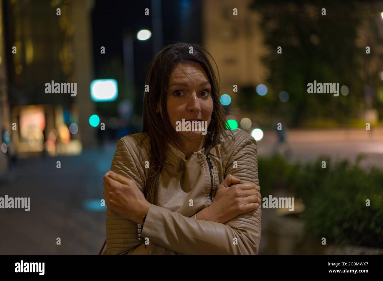 Young beautiful woman is feeling cold downtown at night Stock Photo