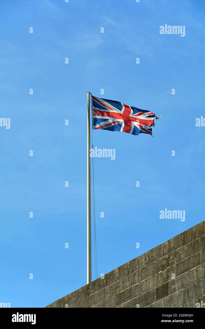 Union Jack flag flying high on a windy day against a plain blue sky. Stock Photo