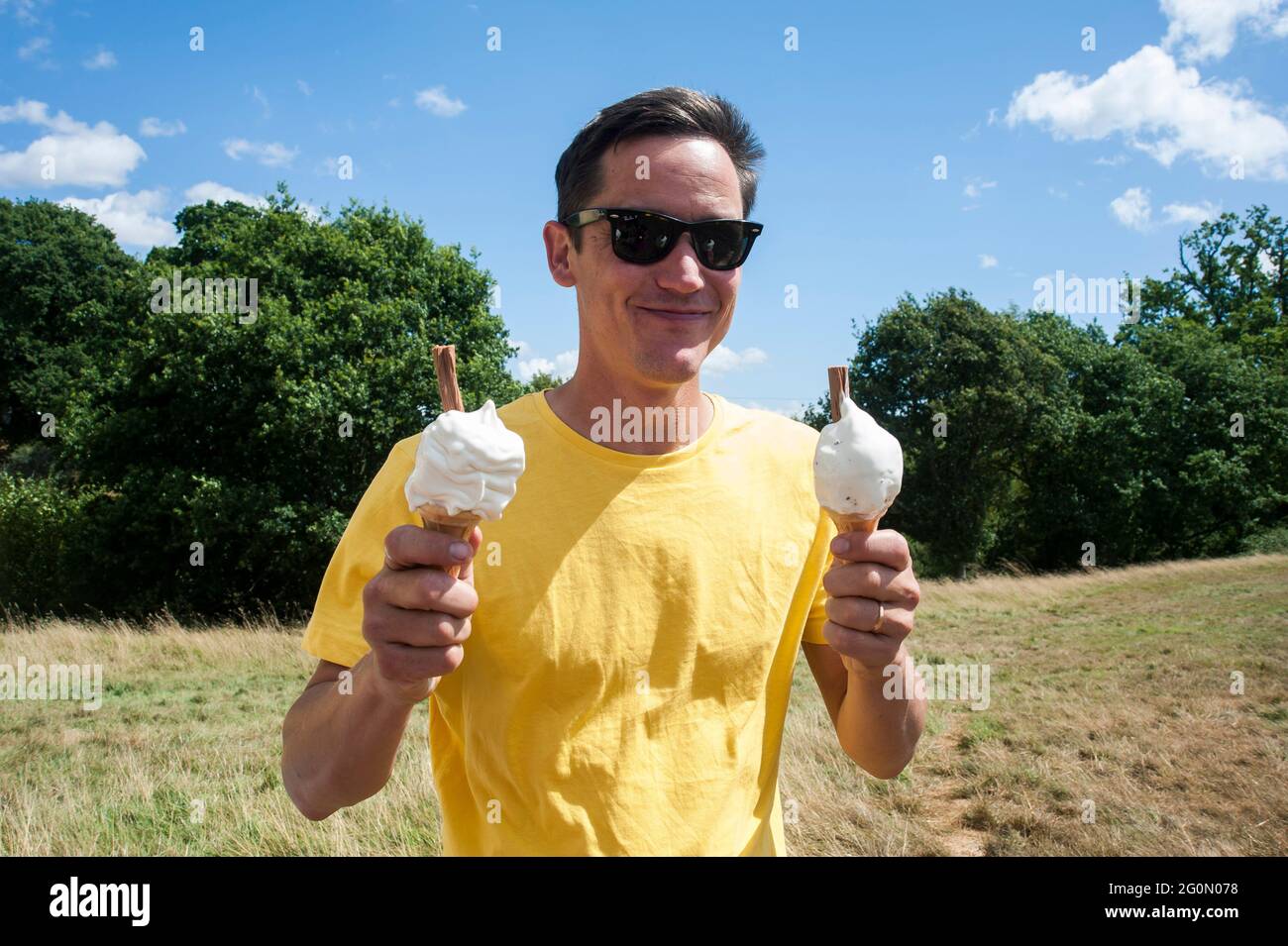 A man holding two ice creams in a field on a hot summers day. Stock Photo