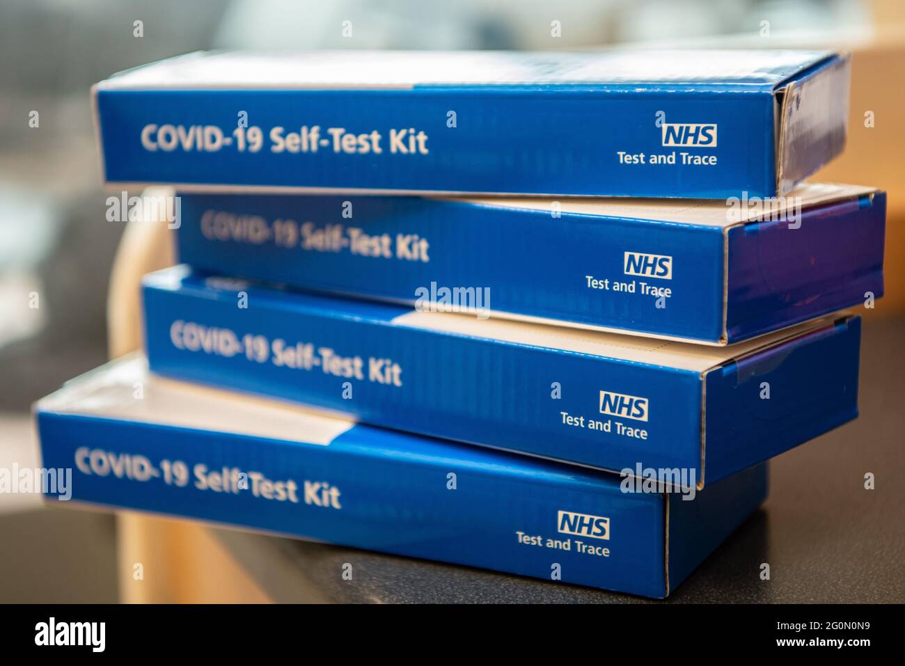 COVID-19 Self-Test Kits stacked in a pile on a table.  Side of the blue COVID test kit clearly showing Stock Photo