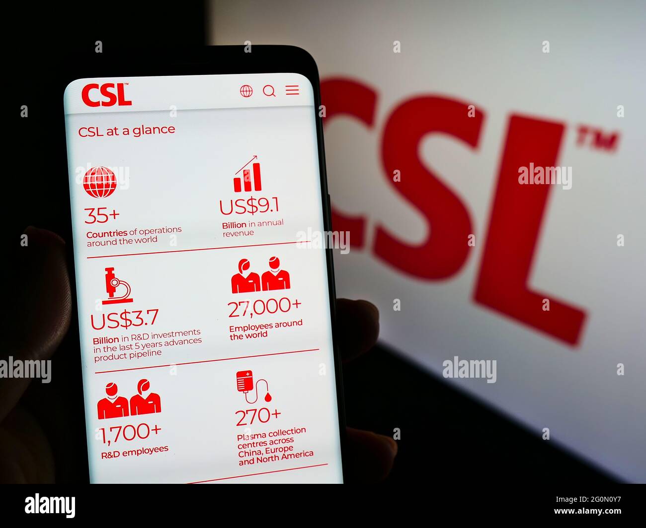 Person holding cellphone with website of Australian pharmaceuticals company CSL Limited on screen in front of logo. Focus on center of phone display. Stock Photo