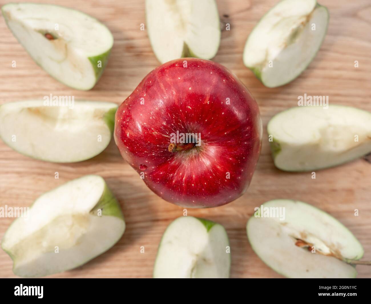 Fresh juicy red apple in a center of light wooden chopping board. Eight quarters of green apple form a circle around red apple. Healthy eating concept Stock Photo