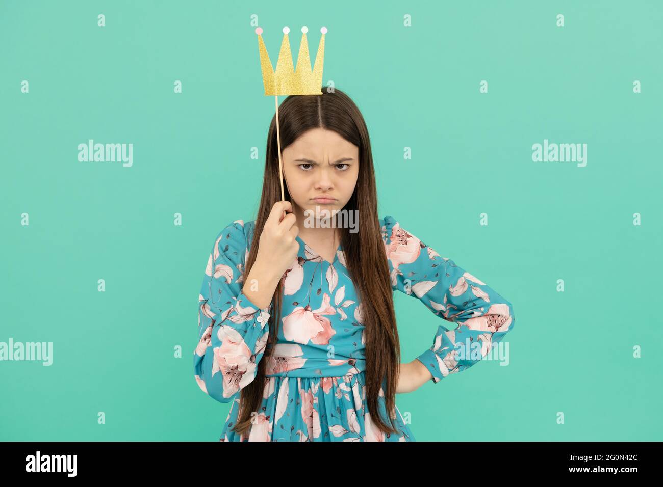 Angry selfish girl hold booth crown over head keeping arm akimbo blue background, egoist Stock Photo