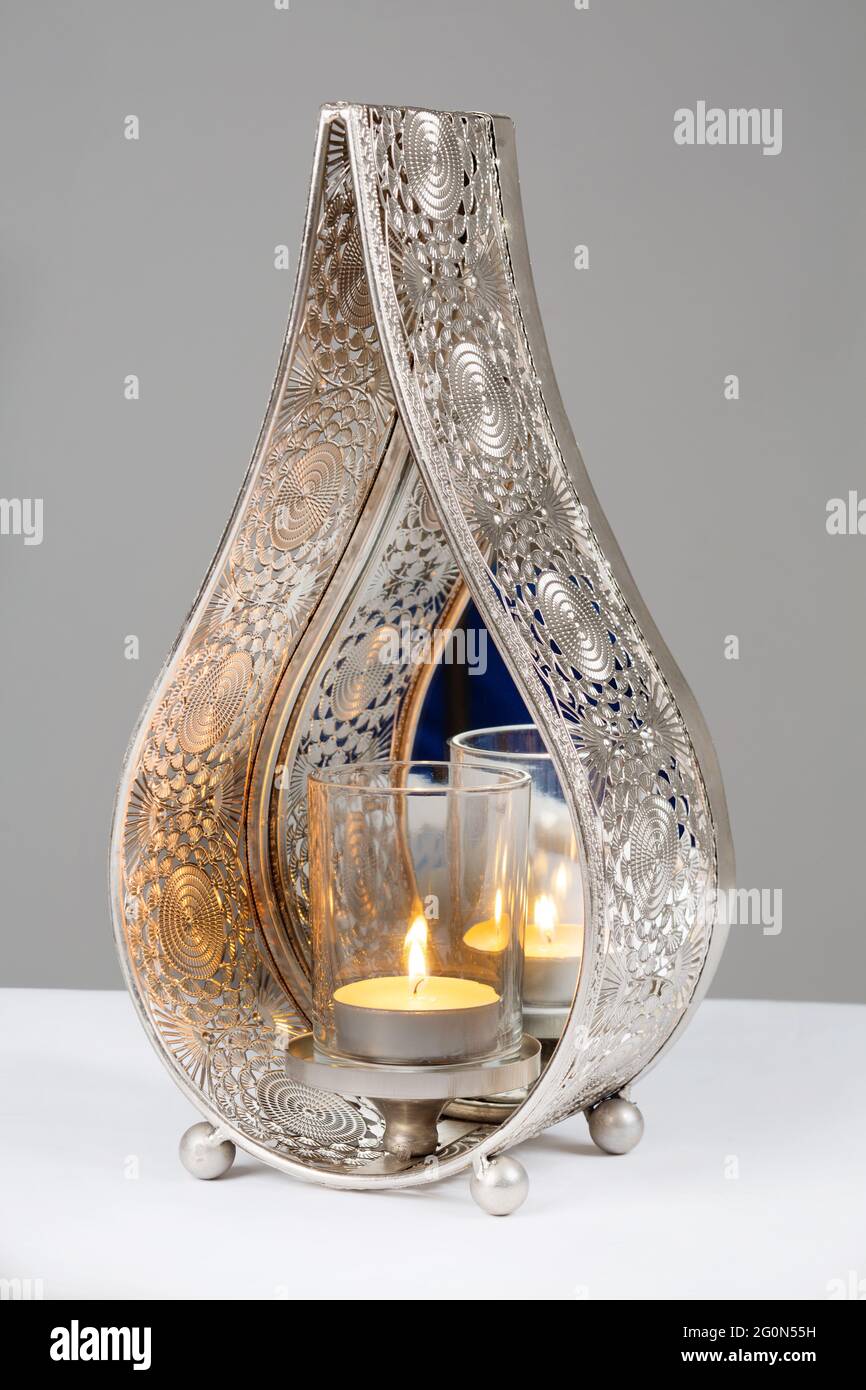 Teardrop shaped shiny metal candle holder with mirror back to reflect light. Stock Photo