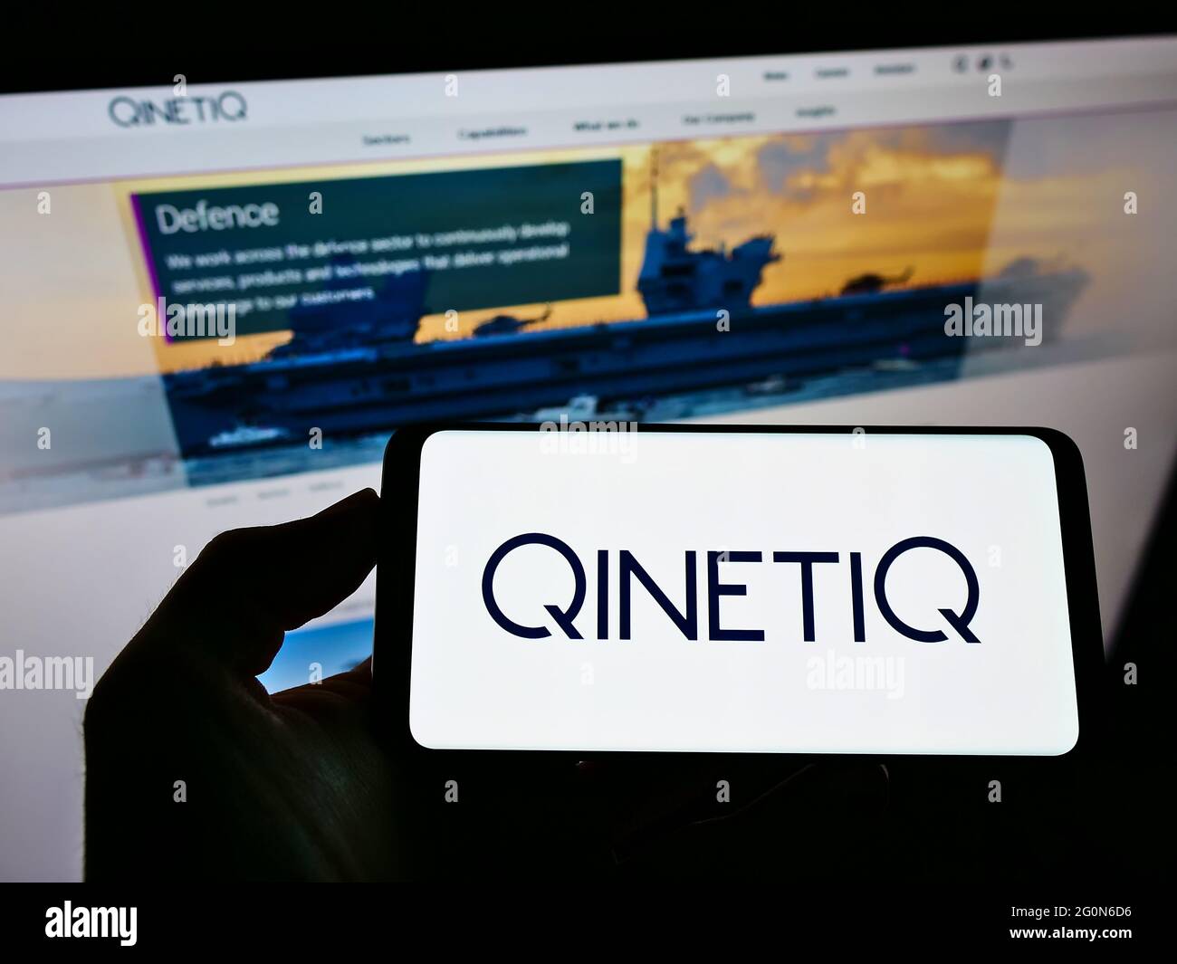 Person holding smartphone with logo of British defence technology company QinetiQ Group plc on screen in front of website. Focus on phone display. Stock Photo