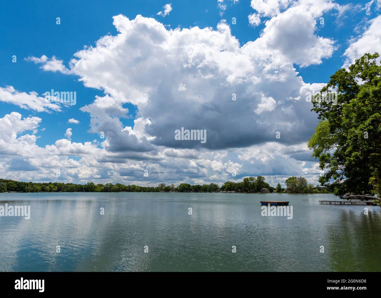 A landscape crop of a Wisconsin Lake (Lower Genesee Lake in Waukesha County).  A swimming raft floats on the calm waters while cumuls clouds are refle Stock Photo