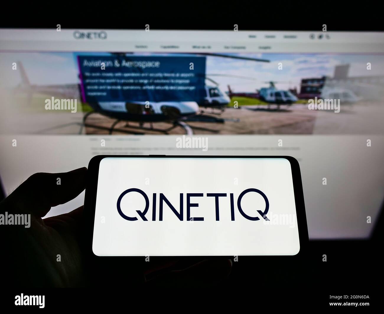 Person holding mobile phone with logo of British defence technology company QinetiQ Group plc on screen in front of web page. Focus on phone display. Stock Photo