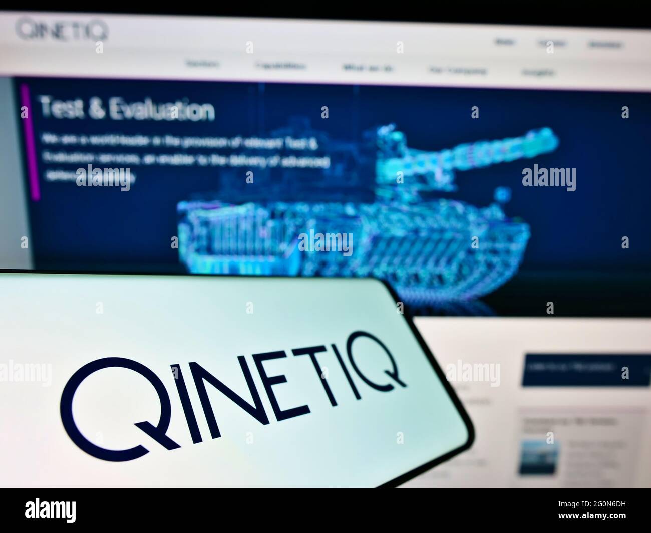 Cellphone with logo of British defence technology company QinetiQ Group plc on screen in front of web page. Focus on center-left of phone display. Stock Photo