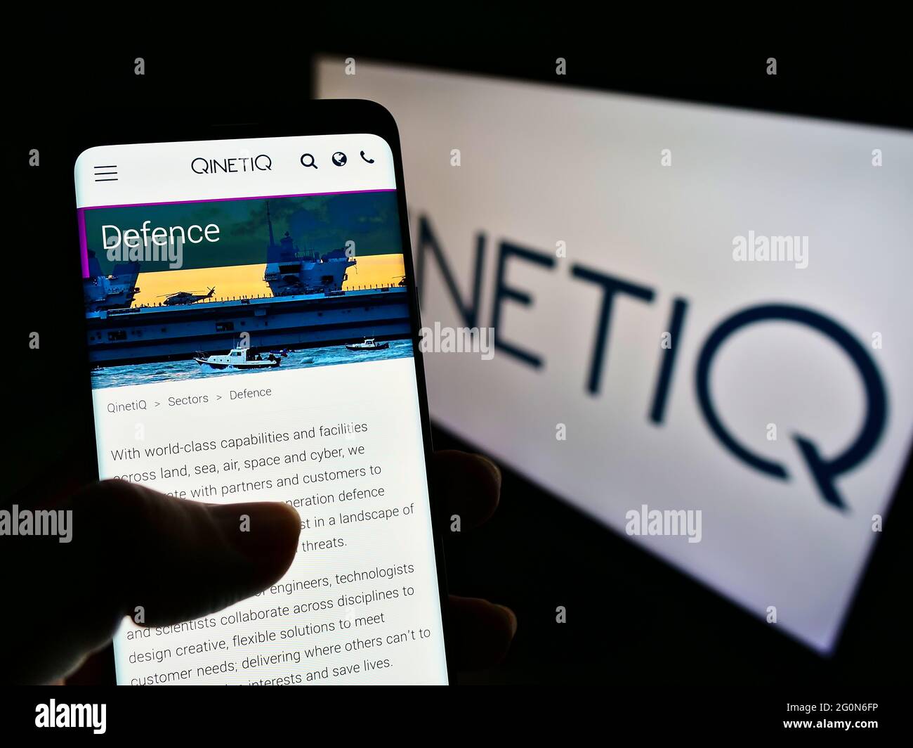 Person holding smartphone with webpage of British defence technology company QinetiQ Group plc on screen with logo. Focus on center of phone display. Stock Photo