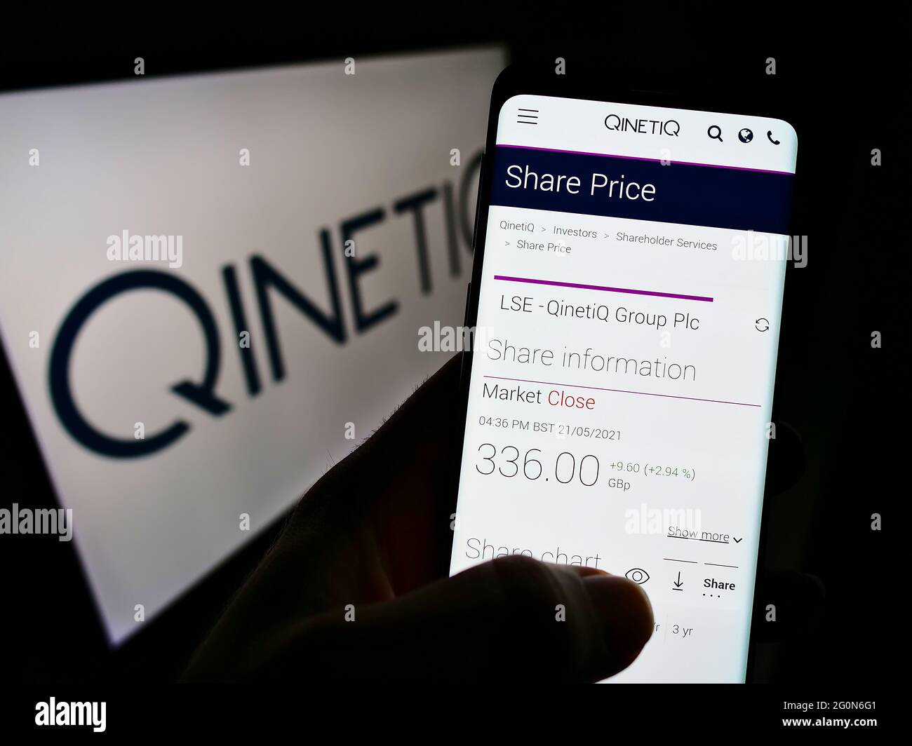 Person holding cellphone with website of British defence company QinetiQ Group plc on screen in front of logo. Focus on center of phone display. Stock Photo