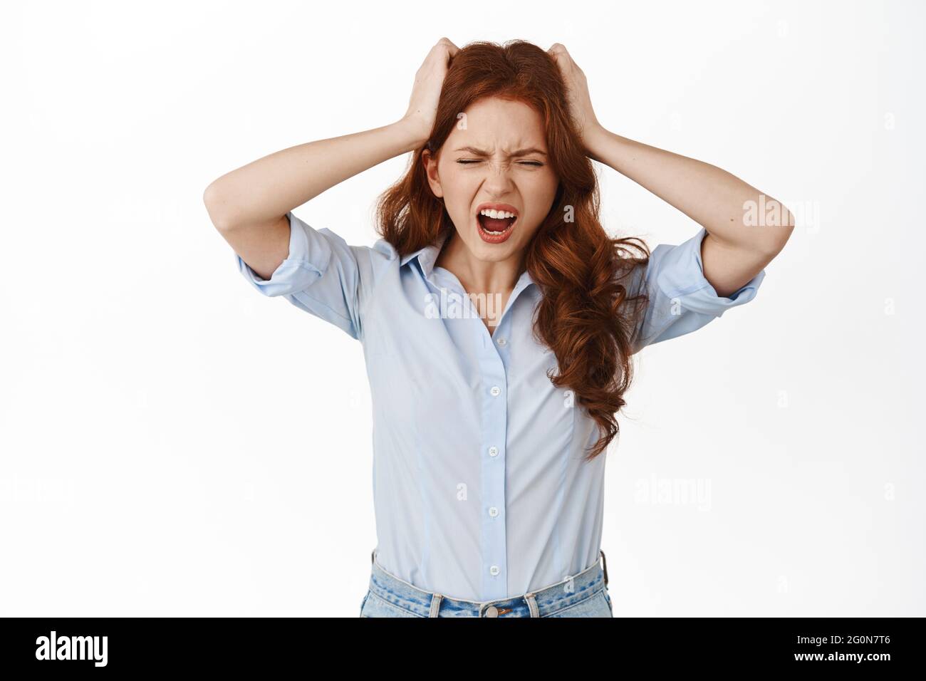 Frustrated redhead business woman scream from tension and distress, holds hands on head troubled, have big problem, losing, standing against white Stock Photo