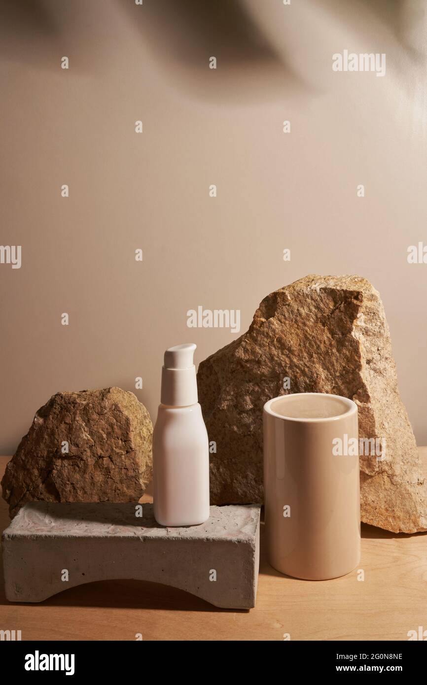 White ceramic opaque bottle on a beige background without labels on natural podium, stones and podium for your product demonstration with tropical plant frame Stock Photo