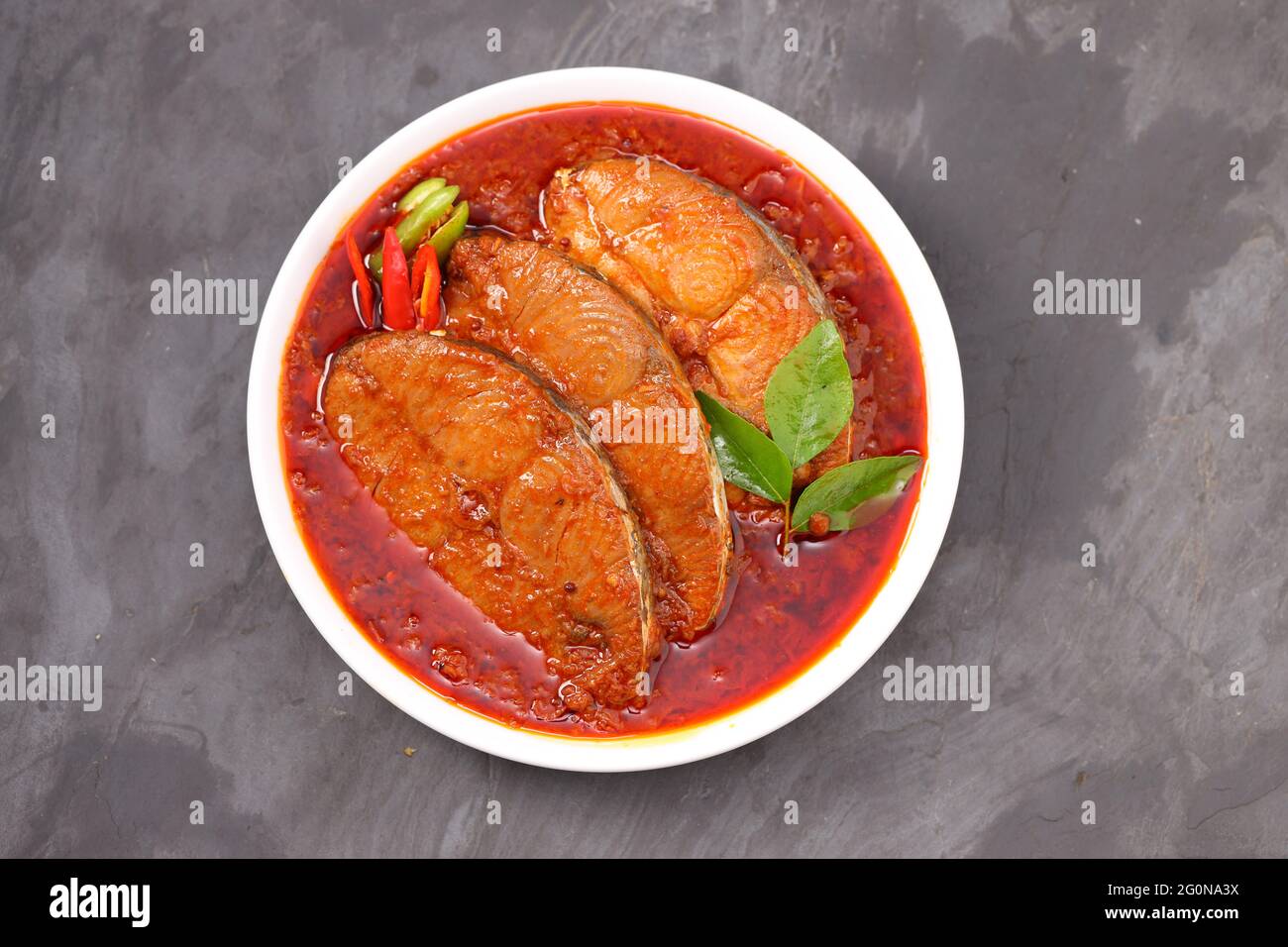 Seer Fish curry, traditional Indian fish curry ,arranged in a white ceramic bowl garnished with curry leaves and fresh chilly on a grey textured backg Stock Photo
