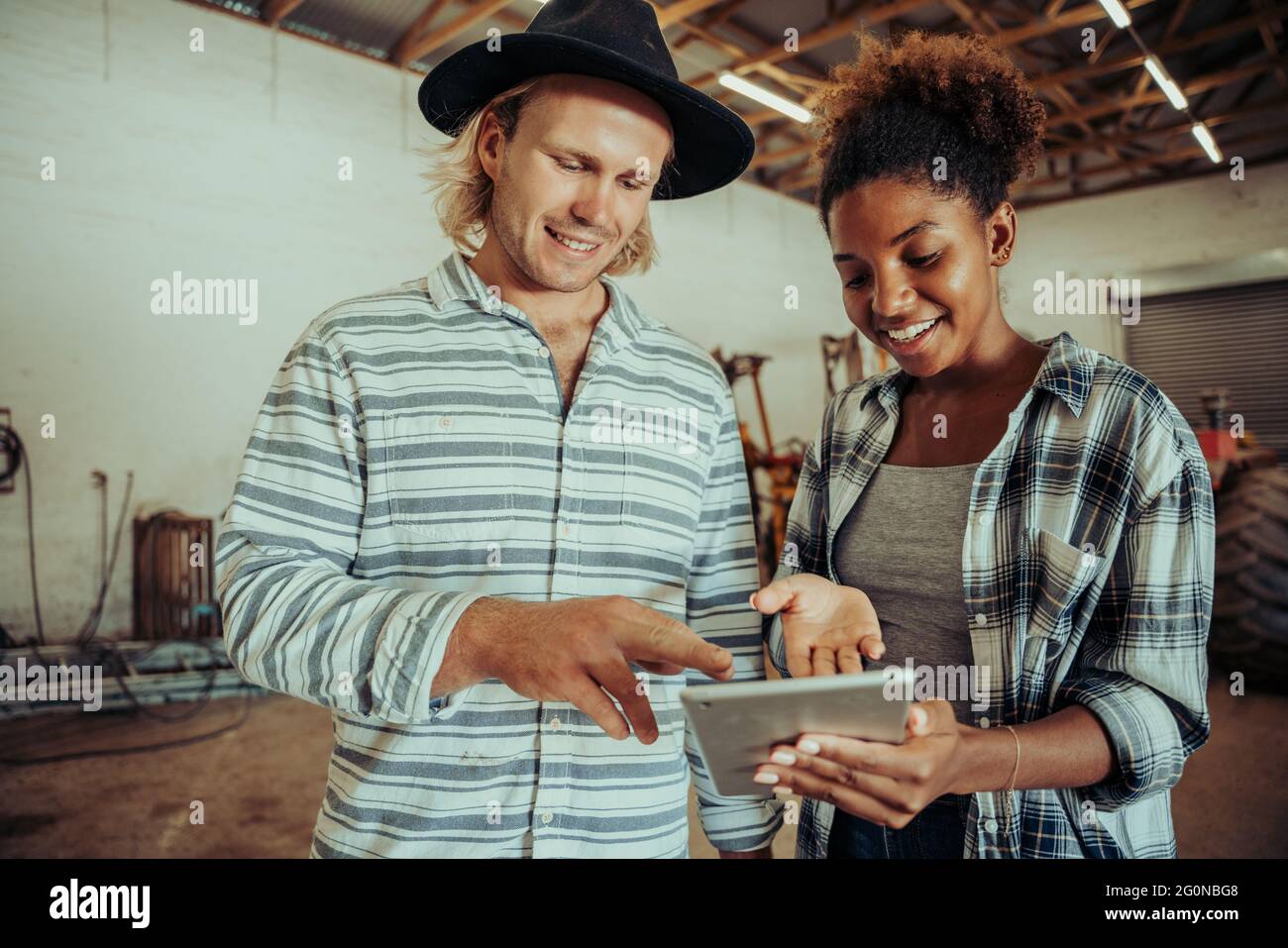 Mixed race couple working on farm project standing in barn typing on digital tablet  Stock Photo