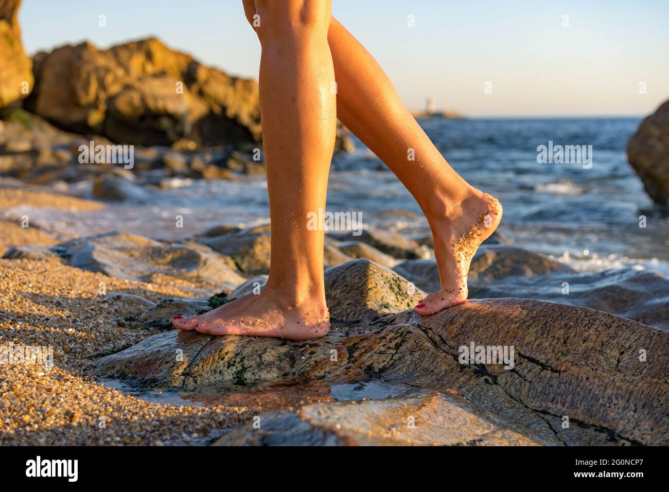 Woman on rock at beach dipping toes in water, having fun outdoor lifestyle in Matosinhos, Portugal Stock Photo