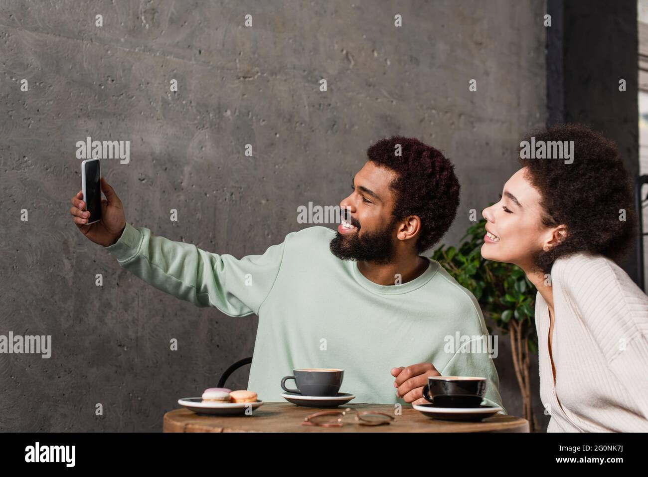 Side view of smiling african american couple taking selfie near coffee ...