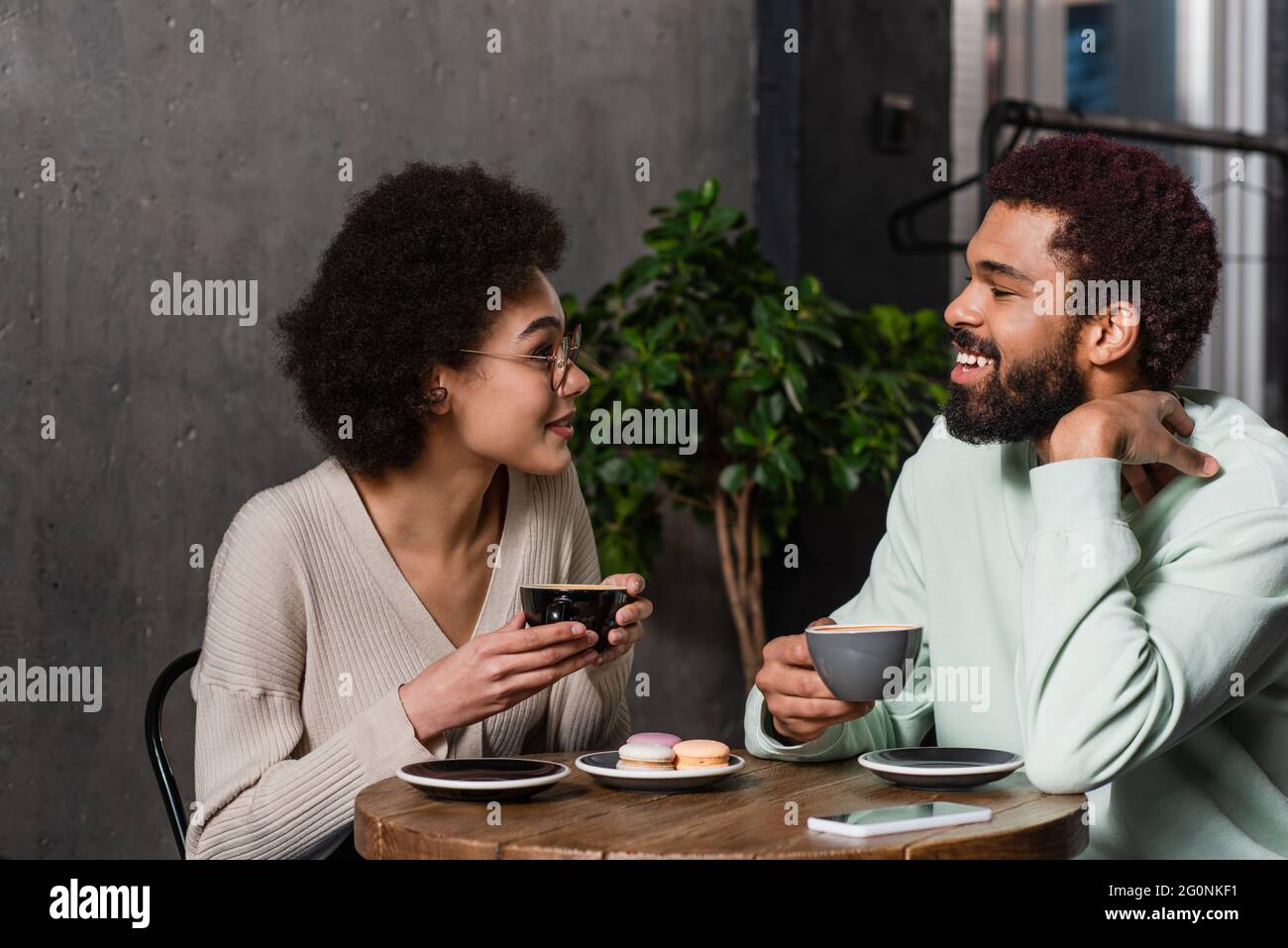 Smiling african american couple with coffee talking near macaroons in ...