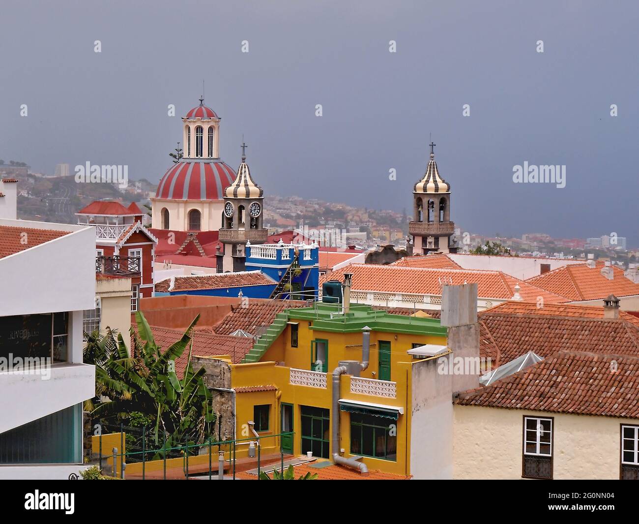 View over the red tiled roofs and the three very different church towers from the town of La Orotava in the north of the island of Tenerife. Pale blue Stock Photo