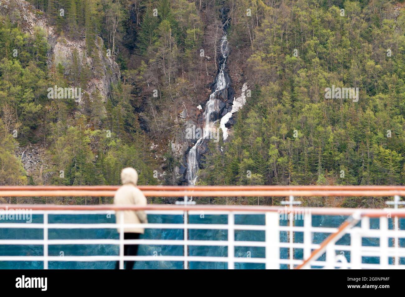 A passenger on a cruise ship looking at a waterfall flowing down a mountainside toward the ocean along the Inside Passage, Alaska Stock Photo