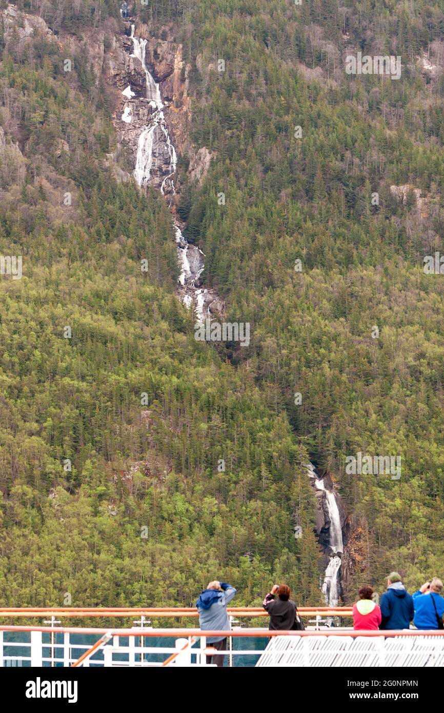Passengers on a cruise ship looking at a waterfall flowing down a mountainside toward the ocean along the Inside Passage, Alaska Stock Photo