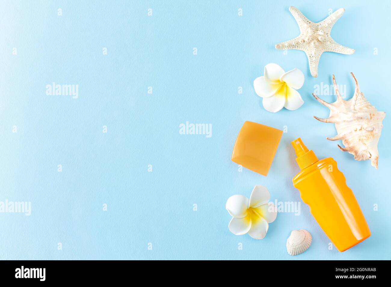 Summer sunscreen, seashells, starfish and frangipani tropical flowers on blue background top view Stock Photo