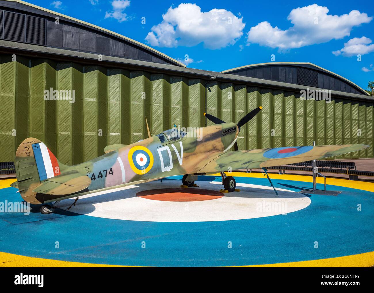 Imperial War Museum IWM Duxford - replica Spitfire static display on RAF roundel base outside a vintage aircraft hangar. Stock Photo