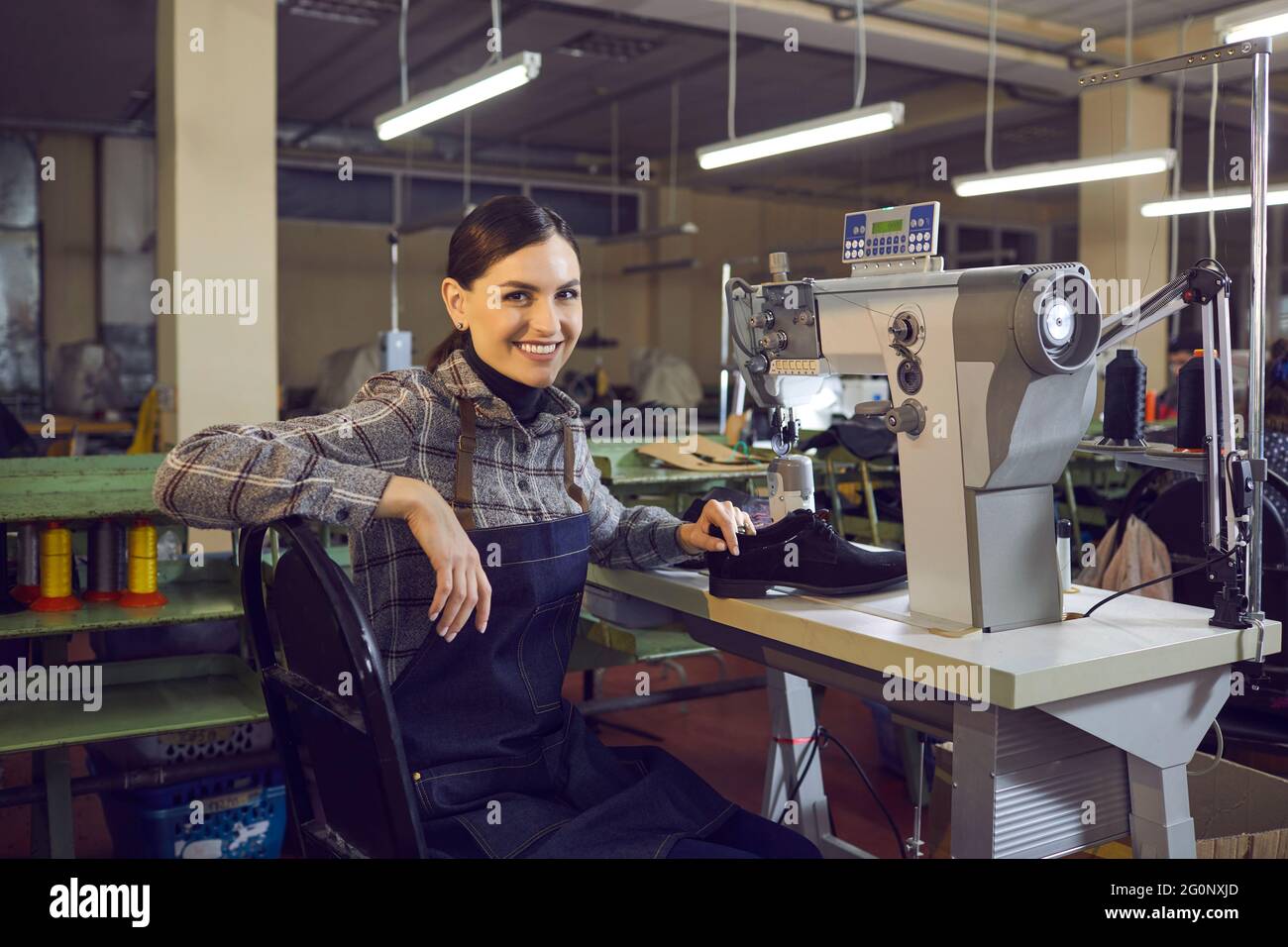 Smiling female shoemaker sitting at workplace looking at camera portrait Stock Photo