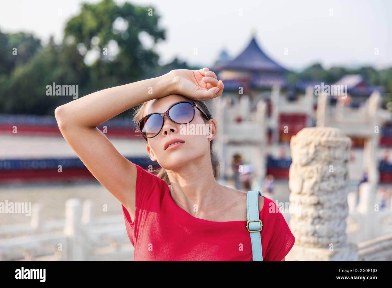 Female asian tourist exhausted during famous attraction visit vacation. Woman wearing sunglassses sweating from sun and heat exhaustion on warm summer Stock Photo