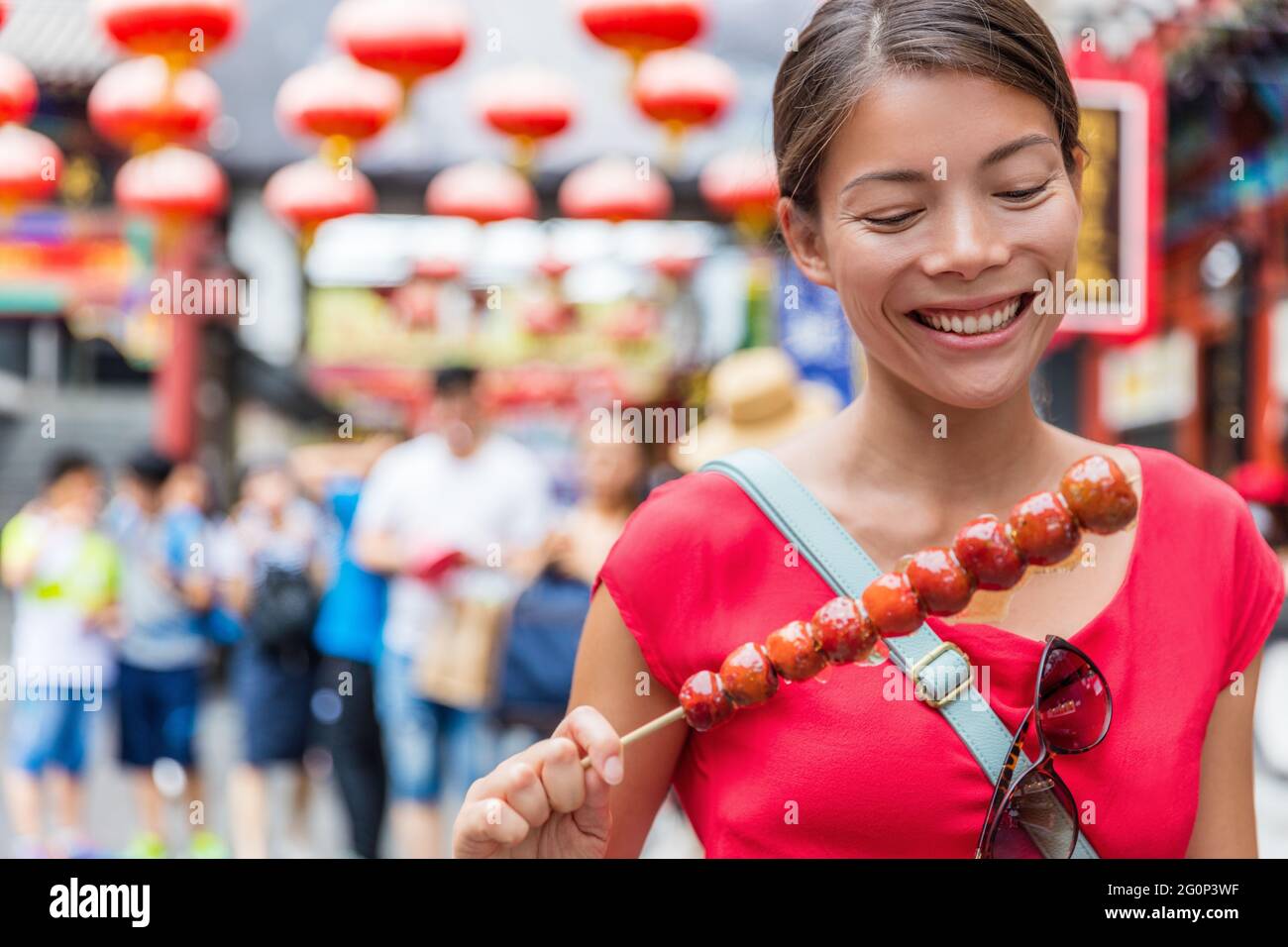 Chinese woman eating Bing Tang Hulu, a traditional chinese food snack from Beijing. Fruit candy stick sold in outdoor market place on Wangfujing Stock Photo