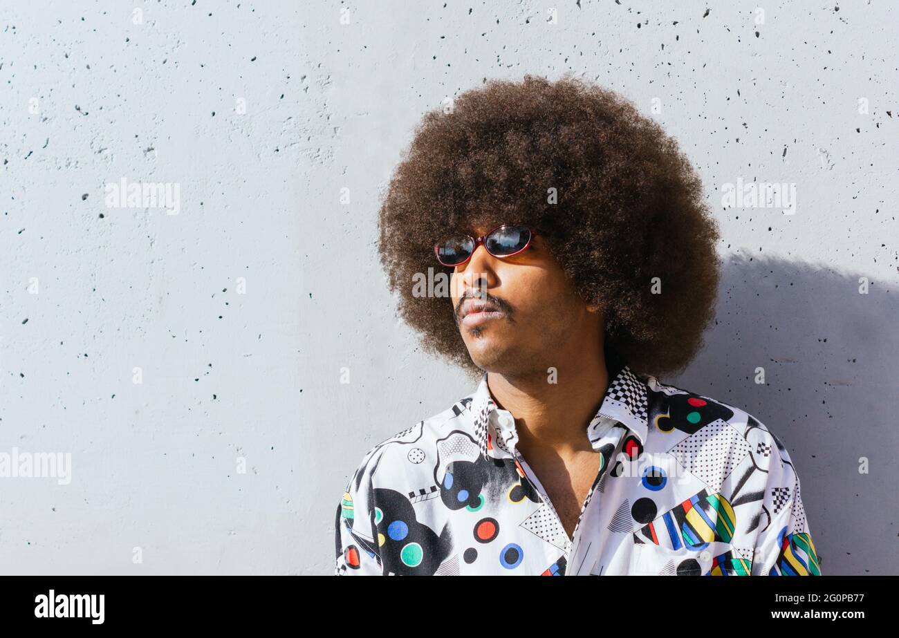 closeup of young black guy with afro hair in white shirt leaning on a  concrete wall painted with warm light Stock Photo - Alamy