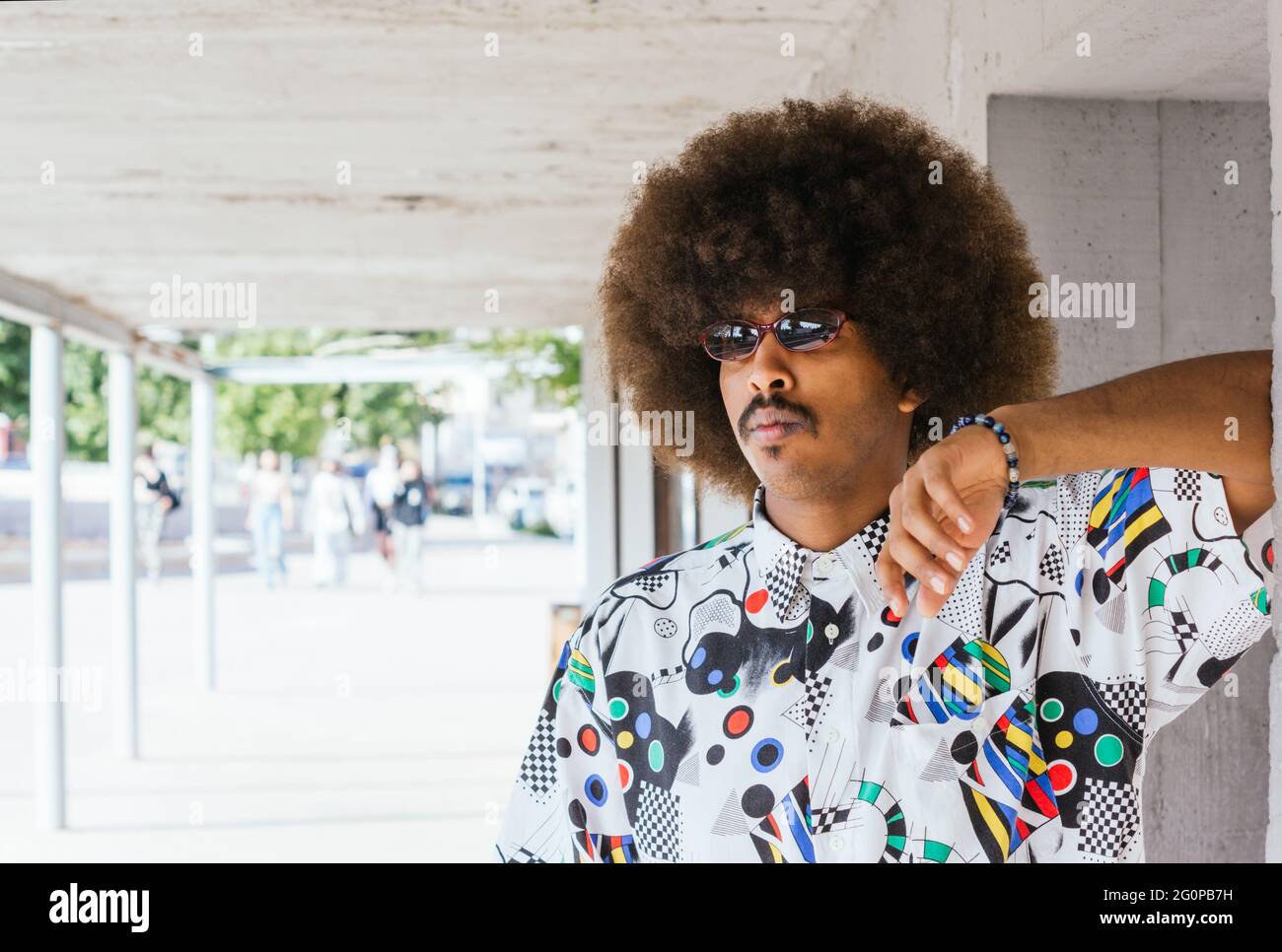 young black guy with afro hair and red sunglasses with white shirt leaning  on a concrete wall with corridor in the background with unfocused people  Stock Photo - Alamy