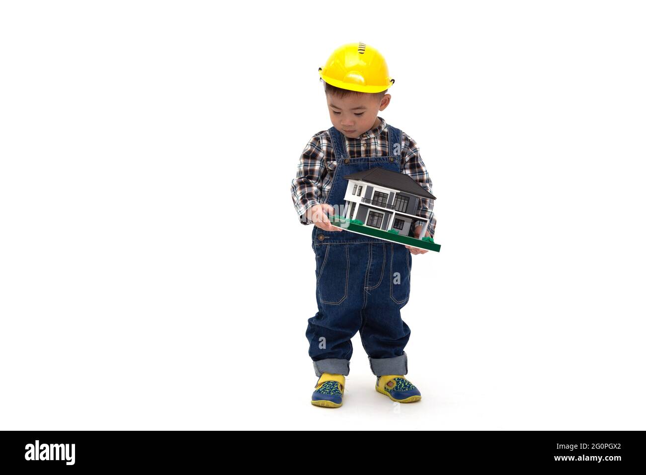 Asian Thai baby boy wearing an engineer suit with hard hat and holding a sample house isolated on white background, Construction worker of real estate Stock Photo