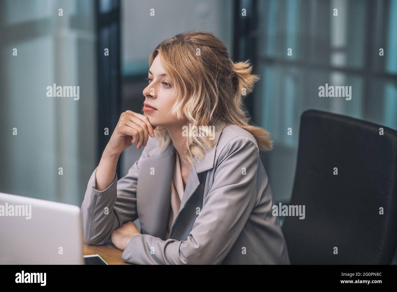 Young adult woman in suit sitting at workplace Stock Photo