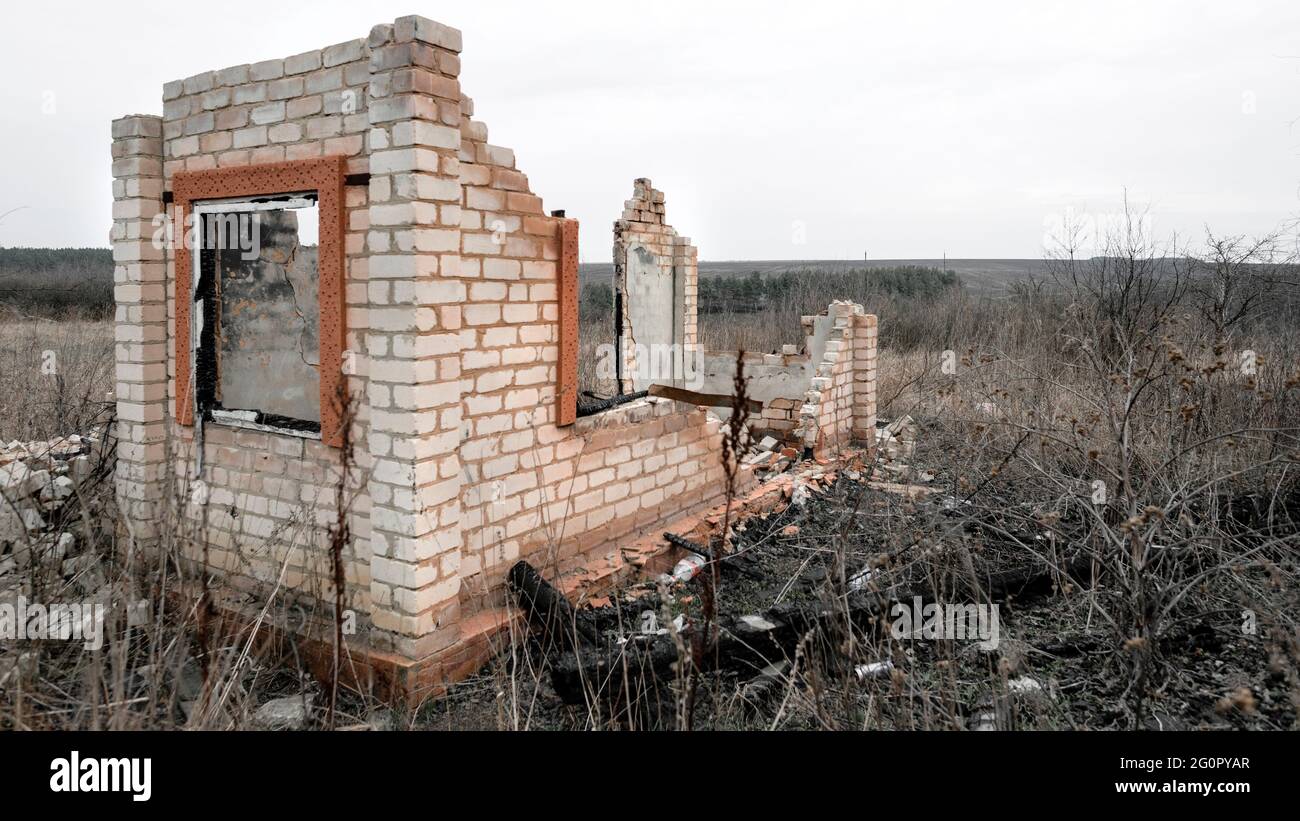 Destroyed and burnt brick structure with a window at the edge of the field Stock Photo