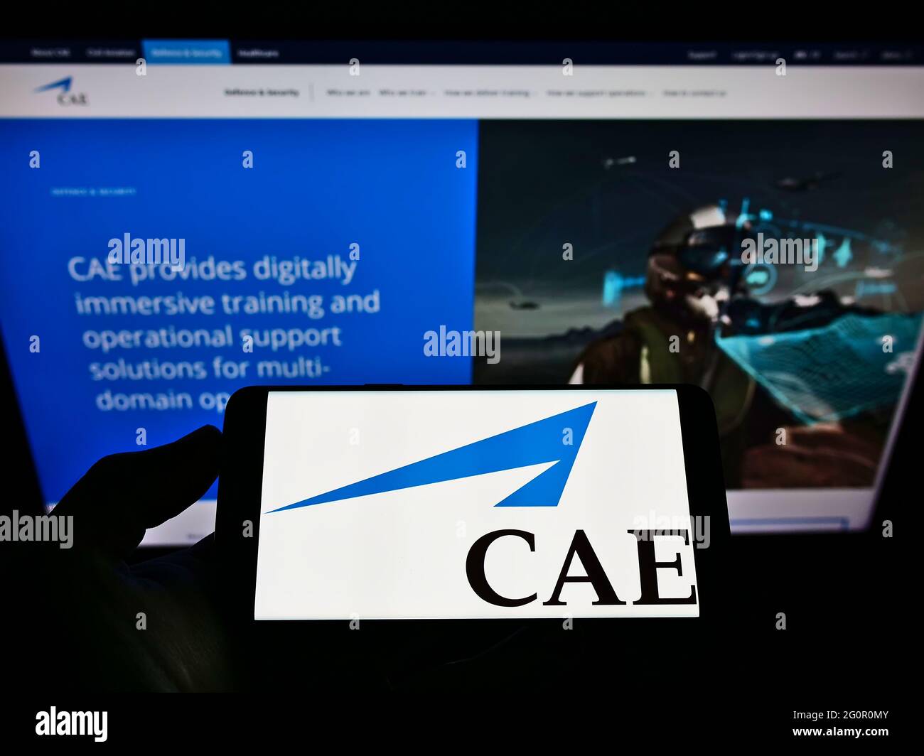 Person holding mobile phone with business logo of Canadian aerospace company CAE Inc. on screen in front of web page. Focus on phone display. Stock Photo