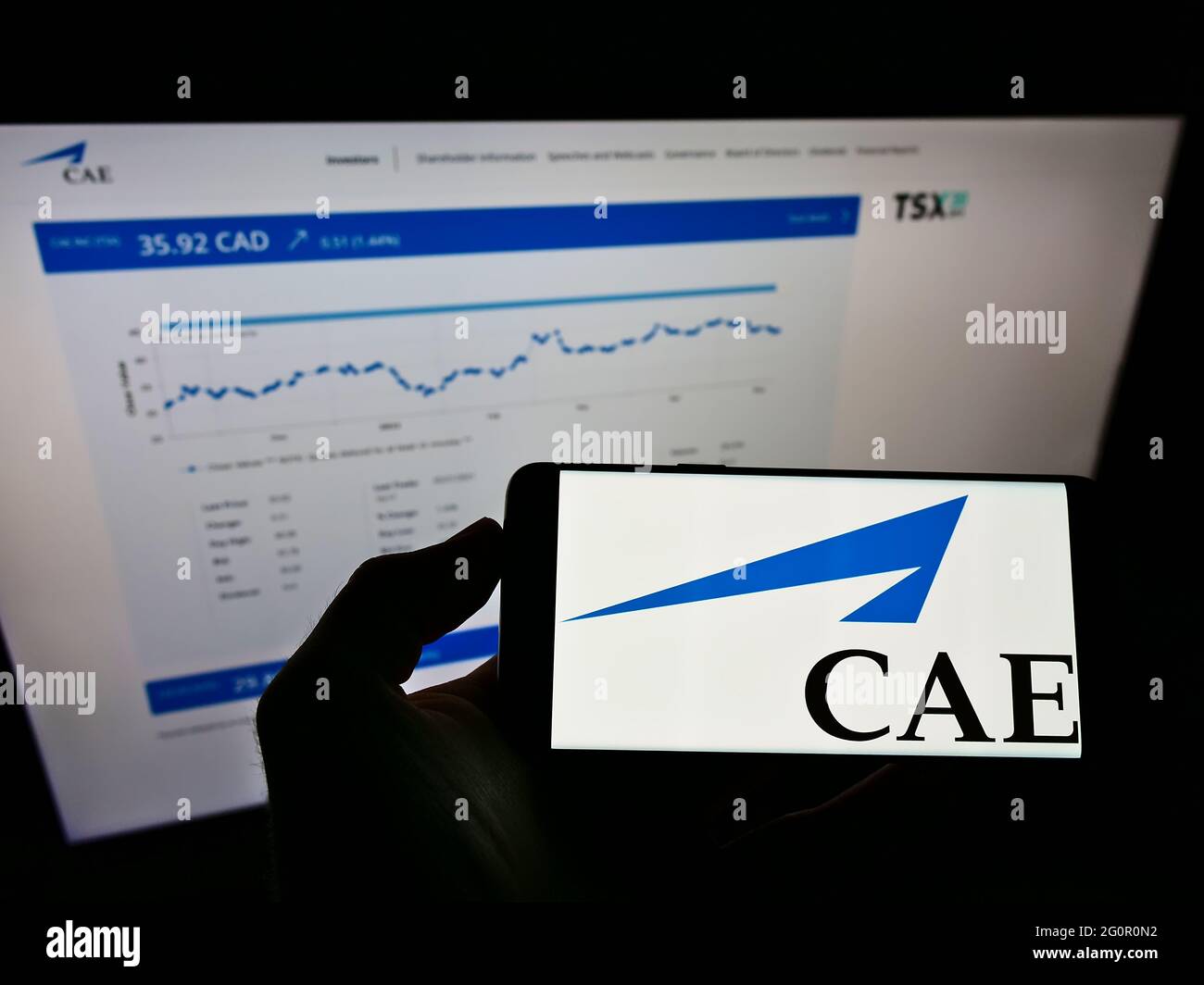 Person holding cellphone with logo of Canadian aerospace company CAE Inc. on screen in front of website with stock chart. Focus on phone display. Stock Photo