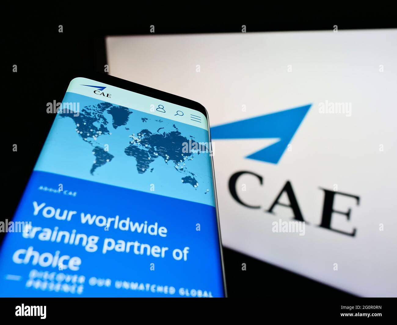 Person holding smartphone with website of Canadian aerospace company CAE Inc. on screen in front of logo. Focus on top-left of phone display. Stock Photo