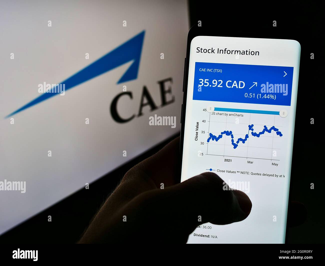 Person holding cellphone with web page of Canadian aerospace company CAE Inc. on screen in front of busniess logo. Focus on center of phone display. Stock Photo