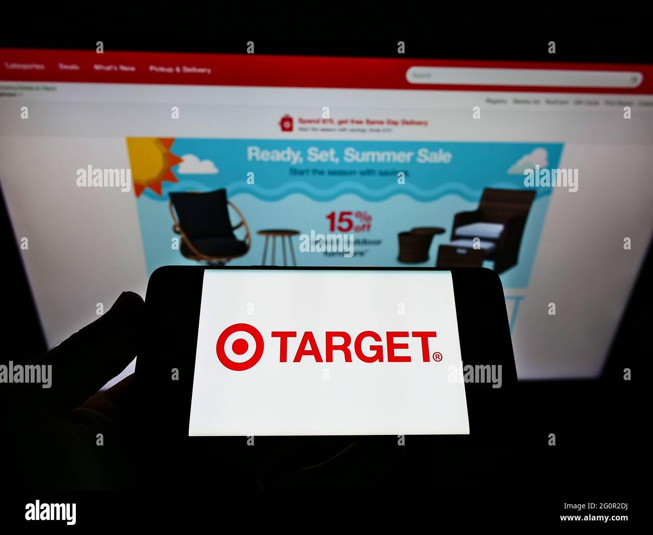 Person holding mobile phone with logo of American retail company Target Corporation on screen in front of web page. Focus on phone display. Stock Photo